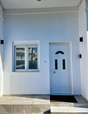 a white building with a blue door and windows at Ivory Escape Apartment - ATH Airport in Spáta