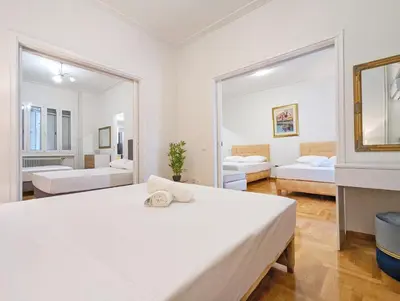 a white bedroom with two beds and a mirror at Casa Divas Grand Palace Apartments in Athens