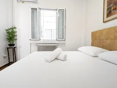 a white bedroom with a large bed and a window at Casa Divas Grand Palace Apartments in Athens