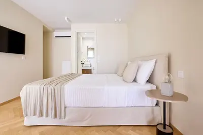 a white bedroom with a bed and a table at The Samirah Luxury Residences in Elliniko in Athens
