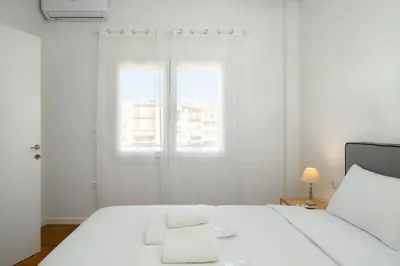a white bedroom with a bed with two towels on it at Bivium Suites by LobbySquare in Athens