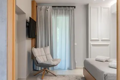 a bedroom with a bed and a chair in front of a window at Aphrodite - Luxenia Suites in Athens