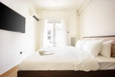 a bedroom with a white bed with a tv on the wall at Spacious 2BR in Koukaki l Balcony l Near Acropolis in Athens