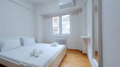 a white bedroom with a bed and a window at A modern and bright apartment in Kolonaki in Athens