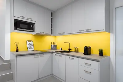 a kitchen with white cabinets and a yellow wall at Acropolis Secret Apartment in Athens