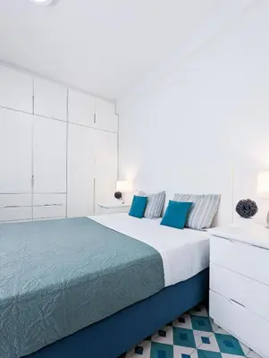 a white bedroom with a large bed with blue pillows at Greek island styled 1BD apt 500m from the sea in Athens