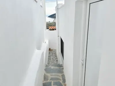 a narrow alley with white walls and a cat sitting in the doorway at Elysian Sunrise Retreat with pool in Porto Rafti