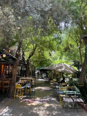 an outdoor cafe with tables and chairs under trees at Koukaki lovely stay in Athens