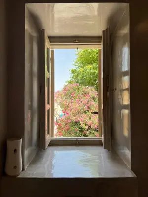 an open window with a view of a flowering bush at One-bedroom Suite - Themelio Suites - Acropolis Area in Athens