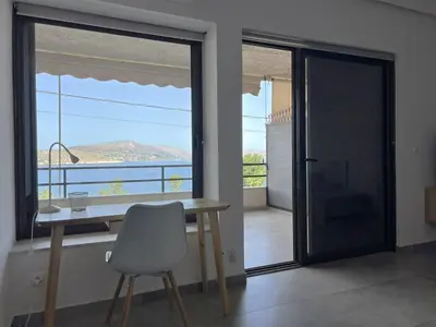 a table and a chair in a room with a window at Beachfront Apartment in Varkiza in Vari