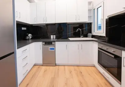 a white kitchen with white cabinets and a wooden floor at Modern flat 7' from Subway Stations in Athens