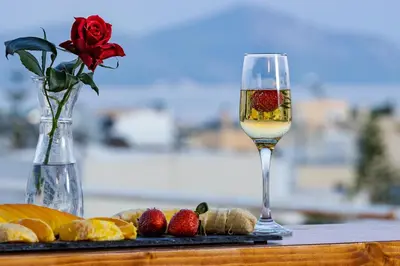 a glass of white wine next to a vase with a rose at Central penthouse studio with Jacuzzi in Varkiza in Vari