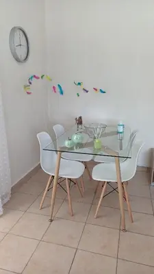a glass dining room table with white chairs and a clock at Armonia's Apartment in Piraeus