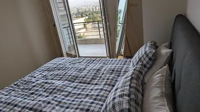 a bed with a checkered blanket in front of a window at Acropolis View Condo, perfect location! in Piraeus