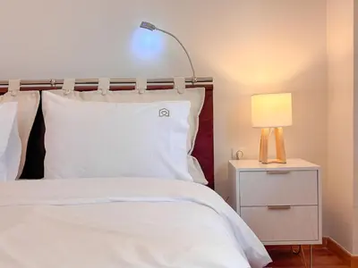 a bed with white sheets and a lamp on a night stand at Restful Flat in Glyfada Center in Athens