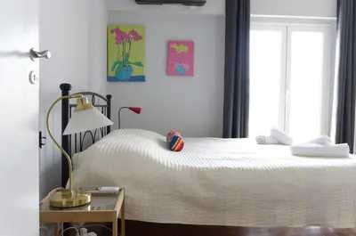 a bedroom with a white bed with a lamp and a window at Funky Apartment in Athens