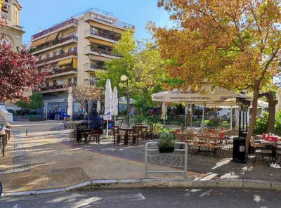 a park with tables and chairs and a building at ARIS Central Kallithea in Athens