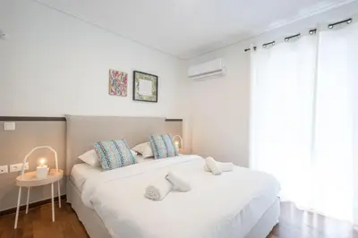 a white bedroom with a large white bed with blue pillows at Seaside Elegance Brand New 2BD Luxury Stay in Athens
