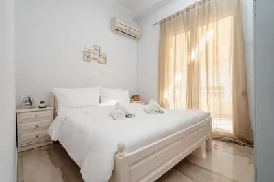 a white bedroom with a white bed and a window at Cozy 1 BR Apt in Koukaki in Athens