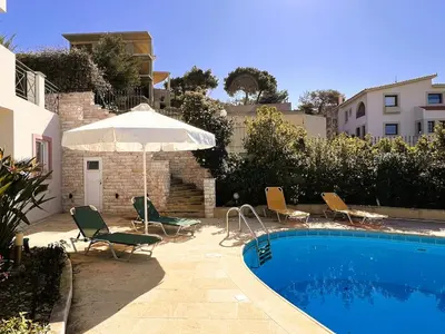 a swimming pool with chairs and an umbrella next to a building at Bella Vista pool Villas in Anavissos in Barbaliáki
