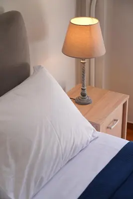 a bed with a white pillow and a lamp on a nightstand at Family Flat for 4 next to the Flisvos Marina by Filos Inc in Athens
