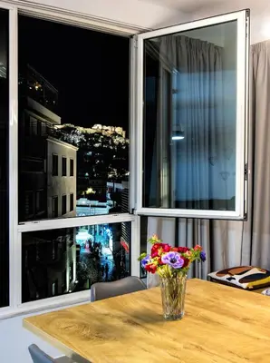 a vase of flowers sitting on a table in front of a window at Chic New Apt with Acropolis View in Monastiraki in Athens