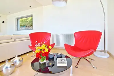 a living room with two red chairs and a table with flowers at Villa TakeOff Saronida in Anavissos