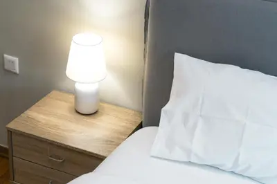 a bed with a white pillow and a lamp on a night stand at Amazing house close to sea in Athens