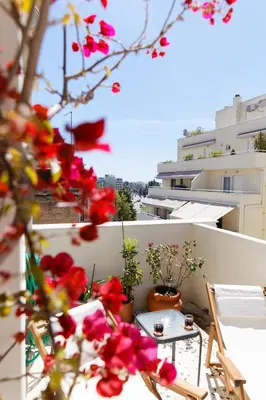 a balcony with red flowers and a table and chairs at Sunny Penthouse For balcony lovers in Athens