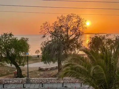 a sunset over a beach with trees and the ocean at Vouliagmeni Kavouri Beachfront Apartment in Athens