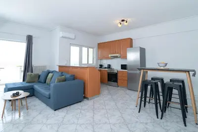 a living room with a blue couch and a kitchen at The Sunrise Apartment By Athens Airport 1 in Spáta