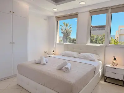 a white bedroom with a large bed with two windows at Beachfront 3bedroom apartment in Porto Rafti