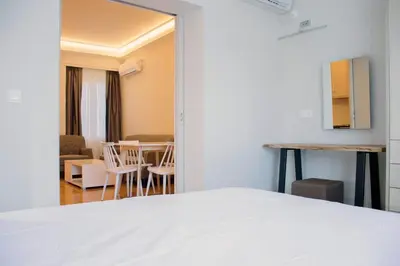 a bedroom with a white bed and a living room at Athens Luxury Apartments Lindos in Athens