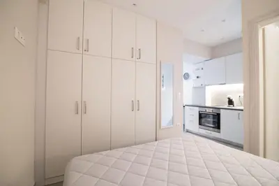 a white kitchen with white cabinets and a bed at Nafsika Cozy Flat A - Glyfada in Athens