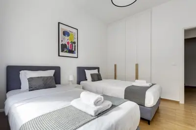 two beds in a room with white walls and wood floors at Cozyopolis - Timeless 3-BR Escape in Athens in Athens