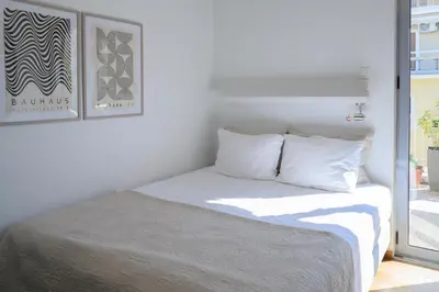 a bed with white sheets and pillows next to a window at Sunbathed Balcony - Philopappou View in Athens