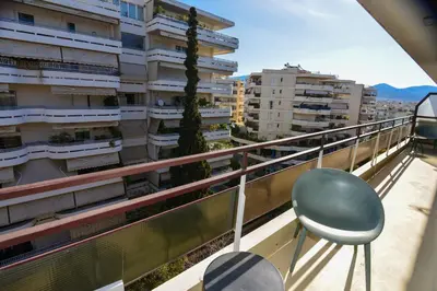 a green chair on a balcony with buildings at Athens stylish apt 2 min walk to the beach , tram in Athens
