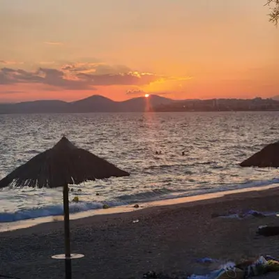a beach with an umbrella and the ocean at sunset at Elaine's Athens Riviera Studios in Athens
