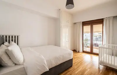 a white bedroom with a bed and a crib at Athenian Living in the Heart of Koukaki in Athens