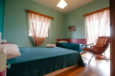 a bedroom with a bed and a chair and two windows at Marousa's Country House 12 minutes from Athens Airport in Koropíon
