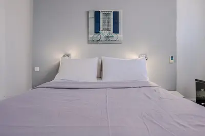 a bed with white sheets and a bike on the wall at Windows with view in Athens