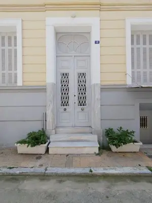 a white door on a house with two potted plants at Apartment Atiki metro shared bathroom and kitchen in Athens