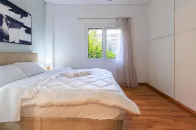 a white bedroom with a large bed and a window at Aiolos Elegant retro suite in GLYFADA centre in Athens