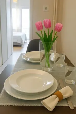 a table with plates and a vase of pink tulips at Saronida BEACH STUDIO in Saronida