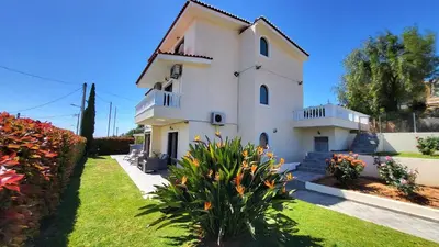 a large white house with a yard with flowers at Villa Golden Sun with swimming pool and jacuzzi in Anavissos