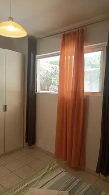 an orange curtain in a room with a window at Cozy lower ground floor apartment by Sea and Tram in Athens