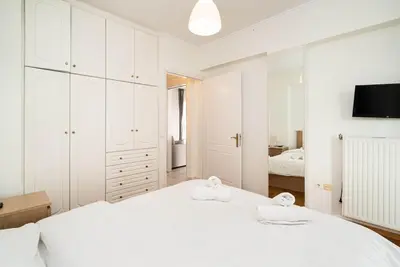 a white bedroom with two white beds and a tv at La Casa De Los Dioses Athens in Athens