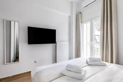 a white bedroom with a bed with a flat screen tv at Les Nuances de Bleu - 1-Bedroom & Balcony in Athens in Athens