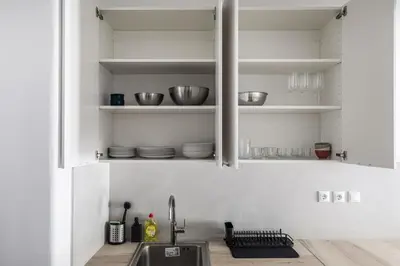 a kitchen with white cabinets with bowls and plates on shelves at Les Nuances de Bleu - 1-Bedroom & Balcony in Athens in Athens