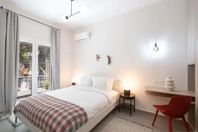 a white bedroom with a bed and a red chair at 1BR Next to Metro Modern Living & Arcade Machine in Athens
